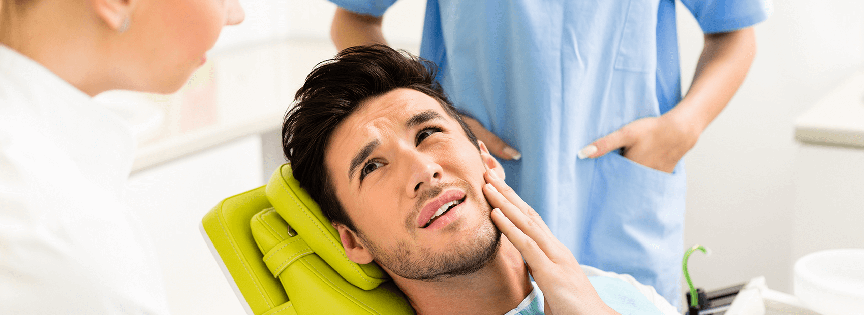 man sitting in a dental chair, holding his jaw in pain